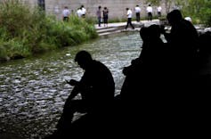 people sit by a stream of water in an urban neighborhood