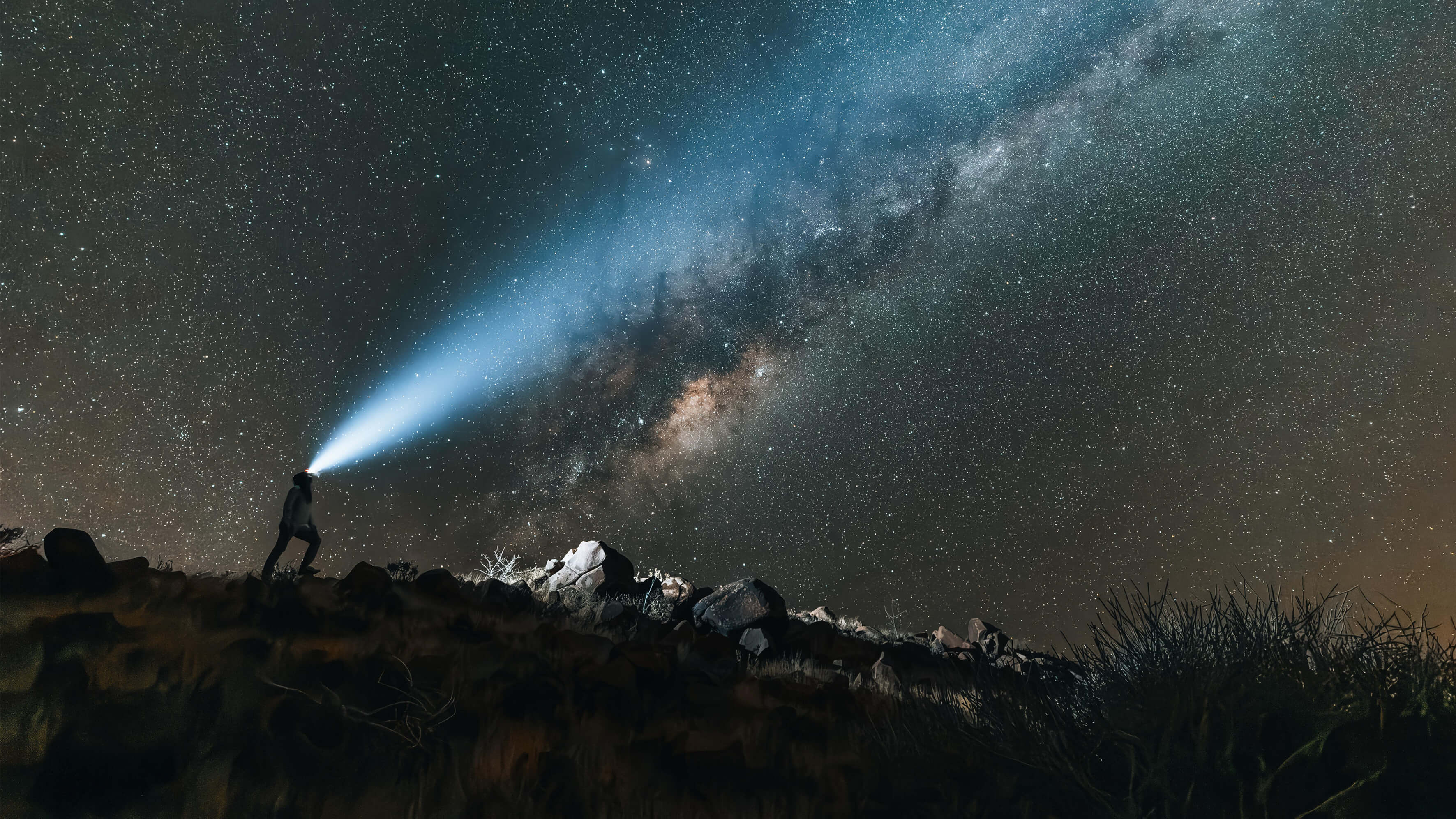 Person wearing headlamp shines beam form lamp towards starry night sky.