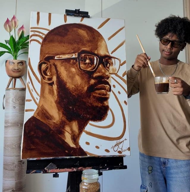 Ricollin Moodley standing next to his painting of Black Coffee made with coffee.