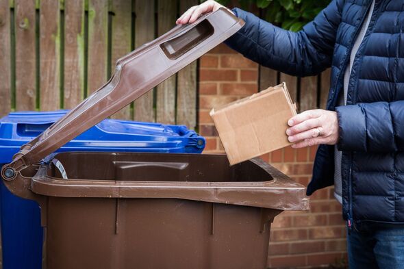 A man recycling cardboard boxes and paper waste in a blue kerb side recycling bin A man recycling cardboard boxes and paper waste in a blue kerb side recycling bin