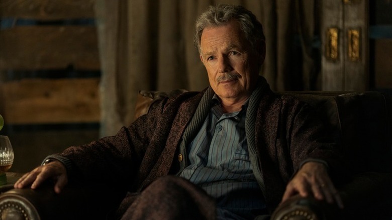 Bruce Greenwood sits in an armchair in 