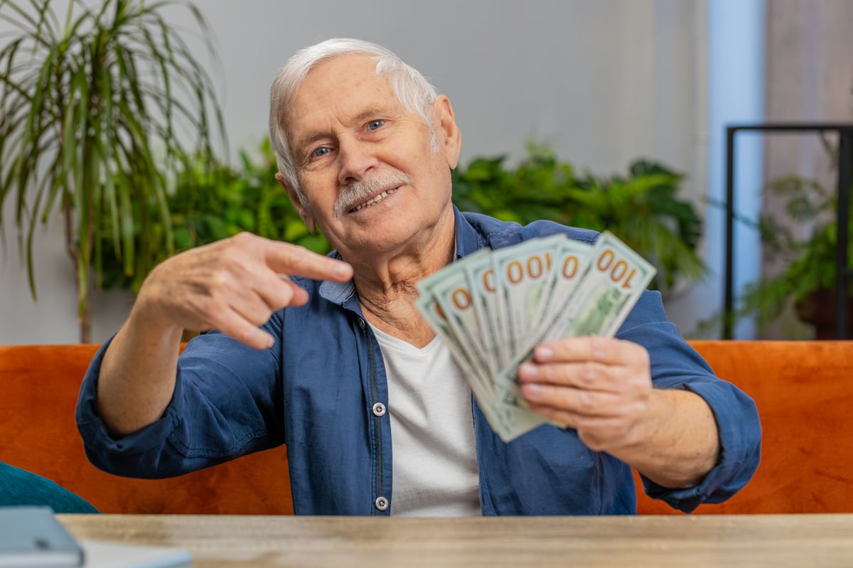 A retired investor is holding several $100 bills, fanned out in his hand.