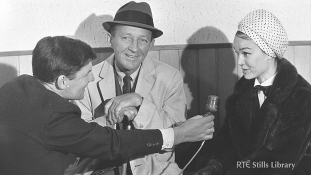 Black and white photo of reporter holding a microphone to Bing Crosby