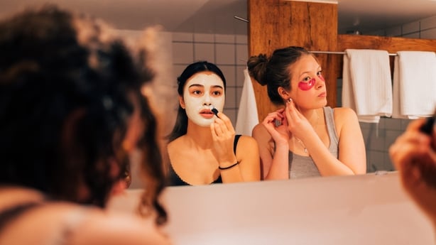 Three young women apply facial masks at home, sharing a relaxing skincare moment in front of a bathroom mirror. Perfect for beauty, wellness, friendship, and self-care themes.Part of a series with video