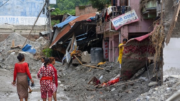 Residents walk past a damaged house in Devighat, Nuwakot, Nepal