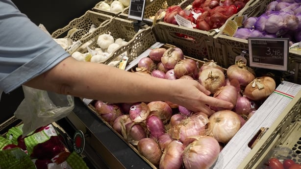 A shopper reaches for onions at a supermarket