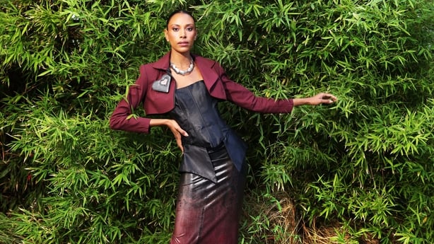 Thais wearing a burgundy cropped jacket, black corset and black / burgundy ombré latex skirt by Alex Lambe. Jewellery is black wooden heart brooch by Clodagh Molloy and necklace by Chloe Van Beck Courser.