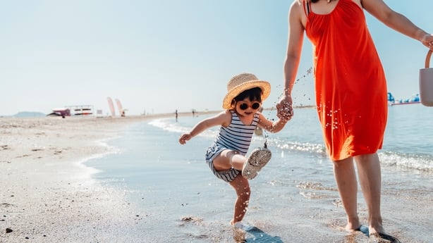 Cropped shot of mother and her little girl walking on the beach against blue sky on a sunny day. Summer family vacation. Motherhood and wellbeing concept.