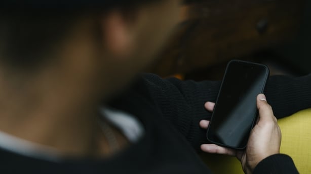Close up of a blurred head in the foreground, looking at his mobile phone and holding it in his hand