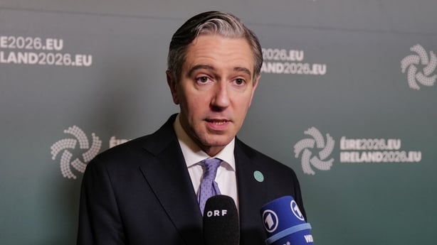 A government minister stands in front of microphones with Ireland EU presidency branding behind him