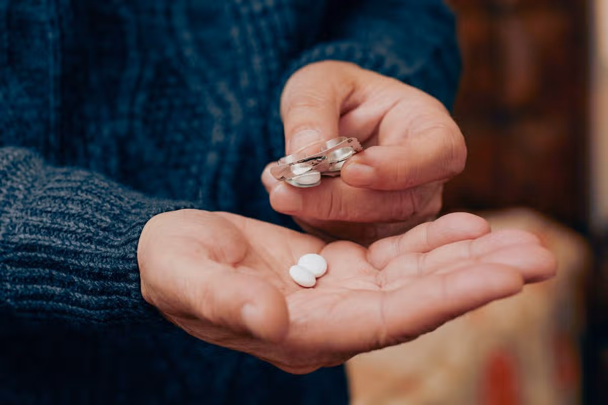 A close-up shot of older man taking a pill from a plastic blister pack.