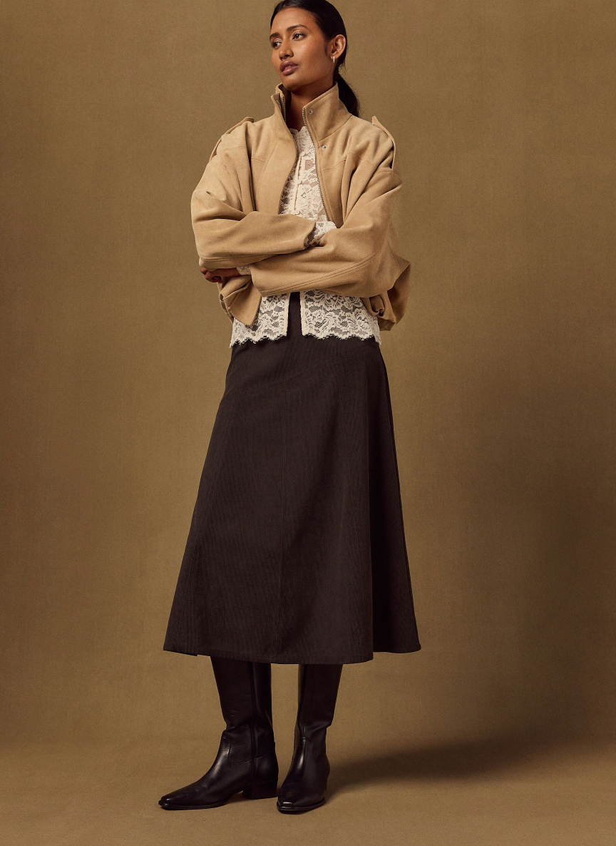 model wearing a beige jacket, lace top, long skirt, and black boots. model wearing a beige jacket, lace top, long skirt, and black boots.