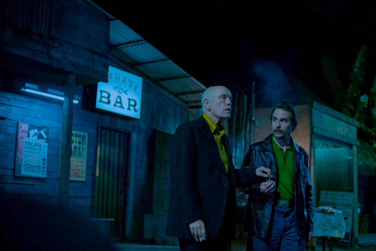 Two men stand beside each other under the night sky outside a bar's entrance
