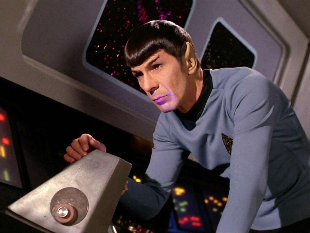 A man with pointy ears and sharp bowl-like bangs looks at a machine