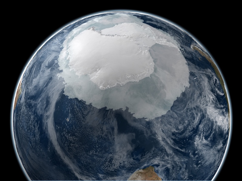 Microbes in Antarctica: About 3/4 of Earth globe with a large part of the upper area covered in white ice, surrounded by ocean and clouds.