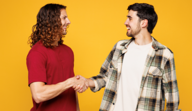 two casually dressed young men shaking hands and smiling