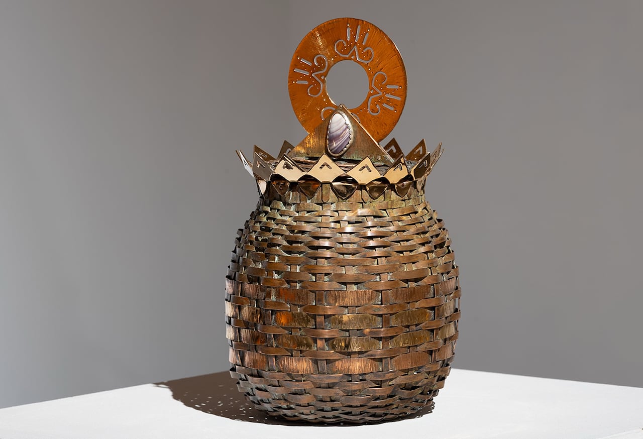 a basket woven of copper and other metals with a decoration and large round copper piece adorning the top