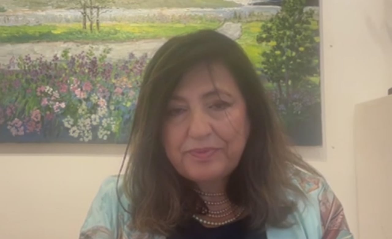 A woman on a video call with a painting hanging on wall behind her.