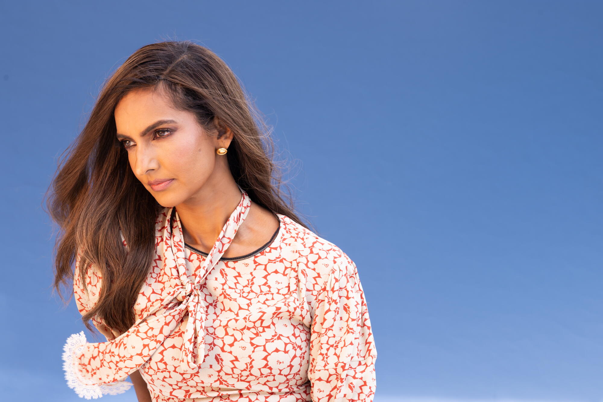 A woman with long brown hair in a floral dress looks downward.