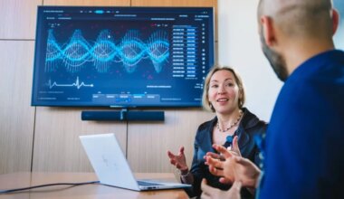 Physician speaking to a colleague in a conference room with a graph displayed on the screen behind her.