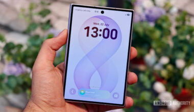 A hand holding the closed Samsung Galaxy Z Fold 8 showing its outer cover display with a digital clock and wallpaper