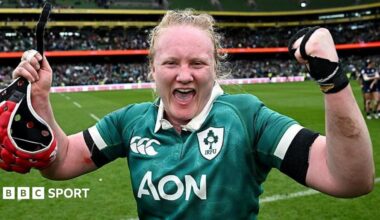 Aoife Wafer celebrates at the side of the pitch with both arms raised and a happy expression on her face, as she wears Ireland's largely green match shirt