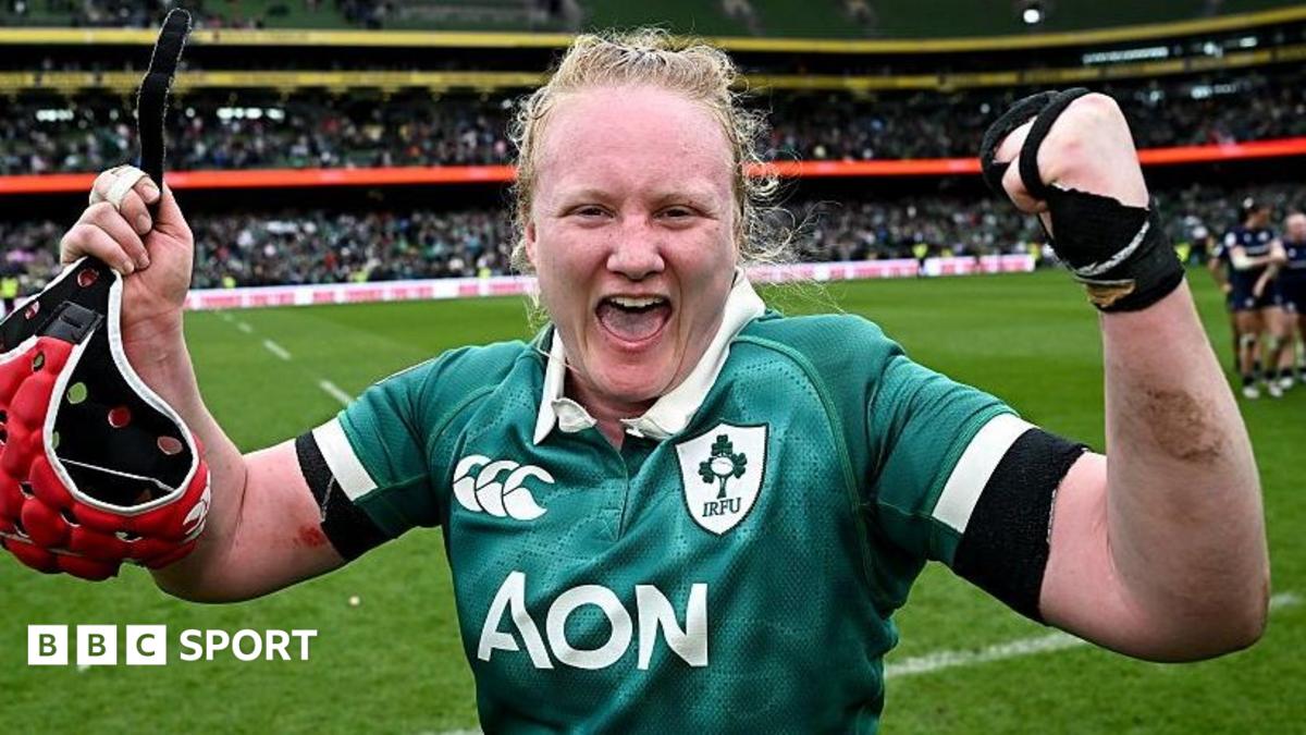 Aoife Wafer celebrates at the side of the pitch with both arms raised and a happy expression on her face, as she wears Ireland's largely green match shirt