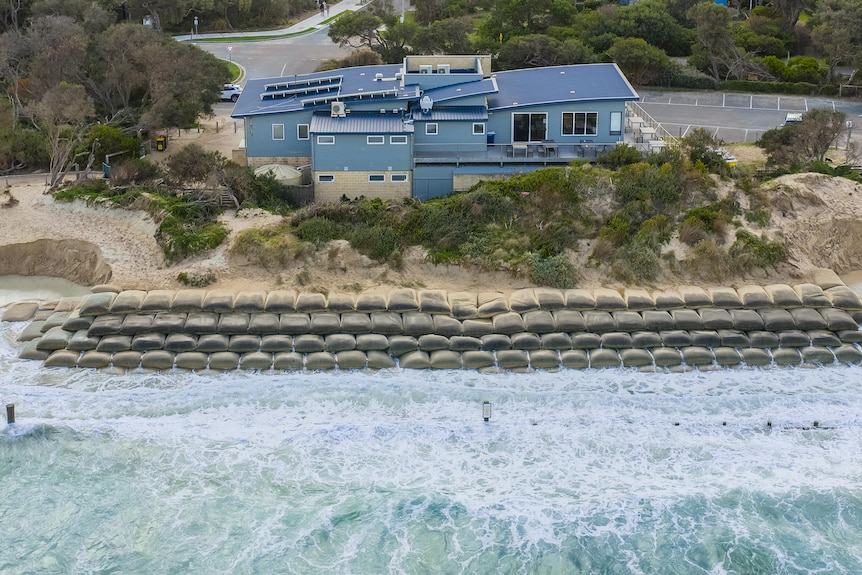 An aerial photo of a beach with sandbags and a lifesaving clubhouse behind