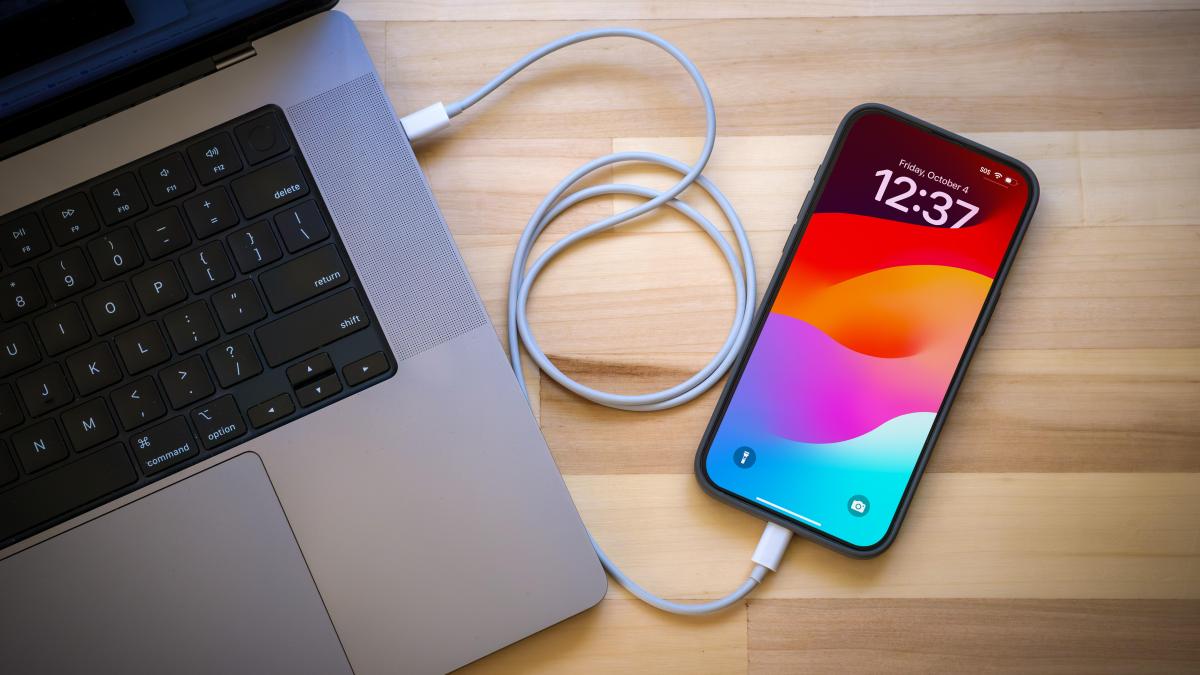iPhone connected to a MacBook Pro laptop via a sync cable.
