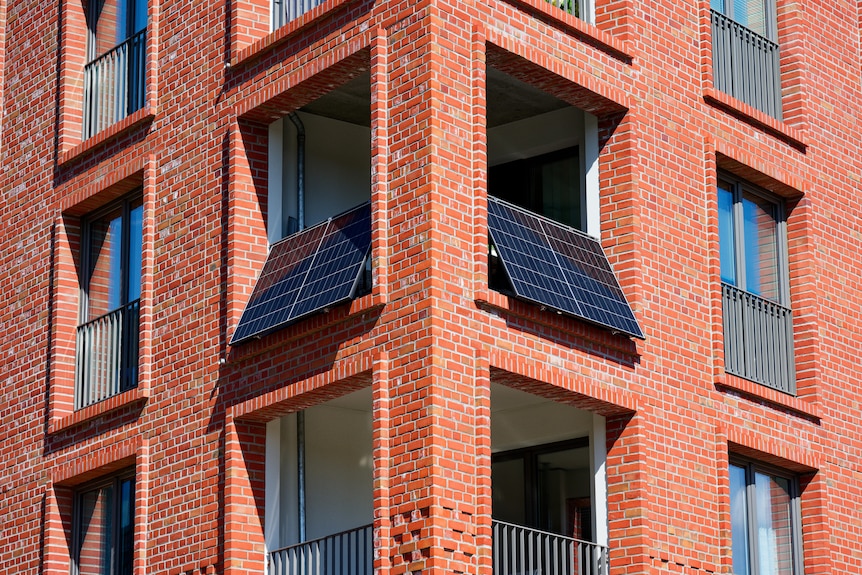 On a tall brick facade a broad balcony spans the window bay solar panels sit along both rails