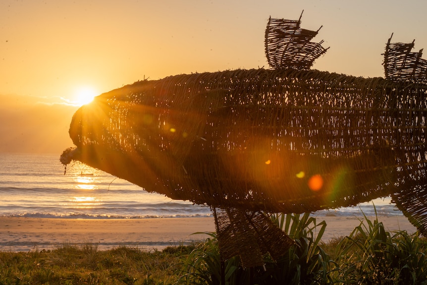 The sun rises behind a massive sculpture of a mullet installed at the beach.