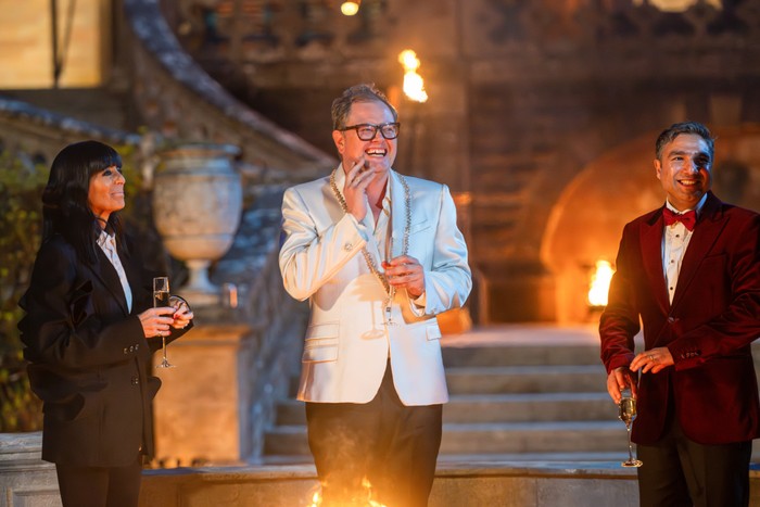 Claudia Winkleman, Alan Carr and Nick Mohammed stood in front of a firepit, laughing and smiling.