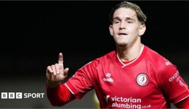 Dom Ballard slides on his knees on the pitch after scoring a goal, while two Bristol City players run behind him