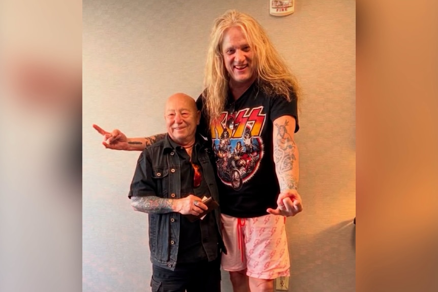 A tattooed older man with a shaved head — Angry Anderson — next to Sebastian Bach, tall, tattoed with long, blond hair.