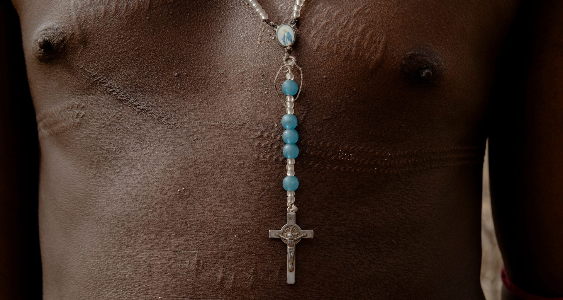 The scarred chest of a Samburu warrior wears a silver and blue rosary.