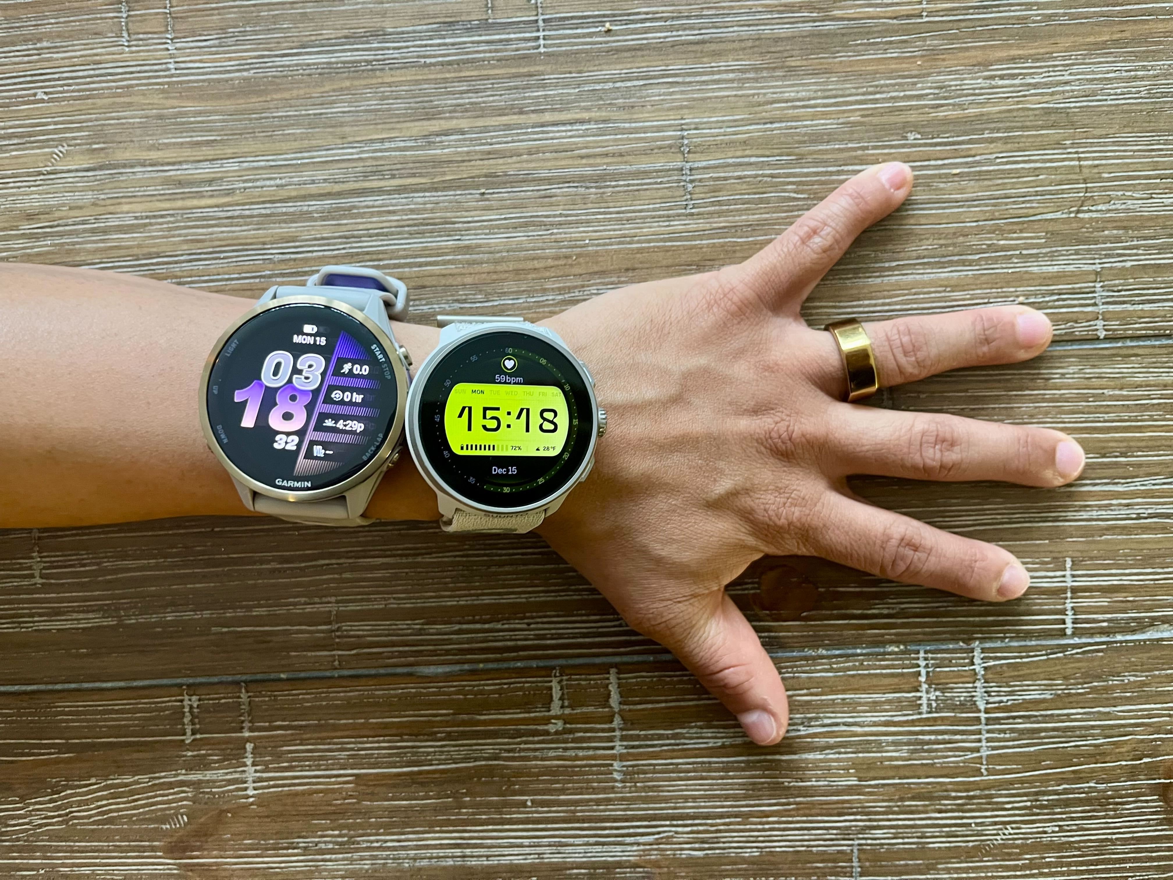 Two fitness tracker watches and a gold Oura Ring on a wrist and finger.