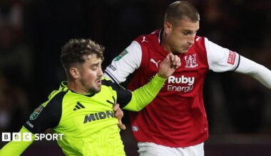 Rhys Norrington-Davies in a bright green Sheffield United away kit is down on his haunches after scoring an own goal