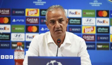 Ismail Kartal, pictured in a white shirt sitting behind a microphone and in front of a blue board covered in colourful sponsor logos