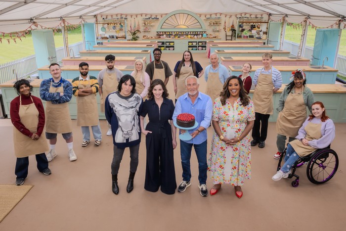 The Great British Bake Off - Series 17 Ep1 The cast, judges and hosts of Bake Off 2026 all stood in the tent looking up and smiling.
