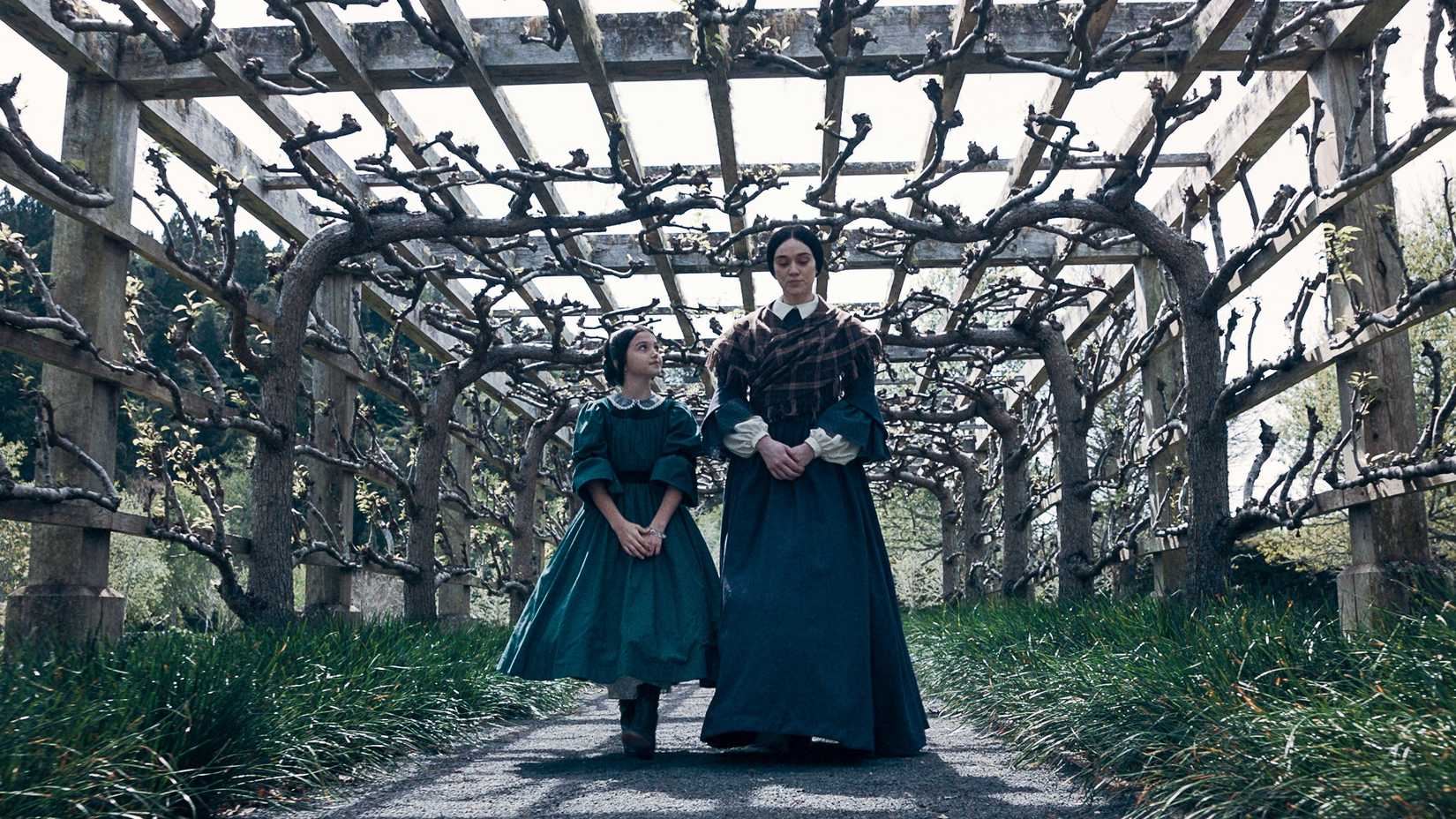 A woman and a young girl walk under a garden canopy