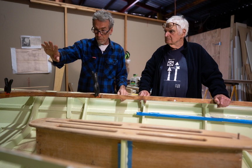 Tony Jones and Matt Dickman look at a boat in a workshop.