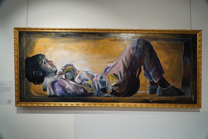 A painting in a gold frame depicts a man dressed in a shirt and trousers lying down on the ground