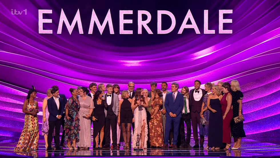 cast of emmerdale on stage under purple lights at tv event