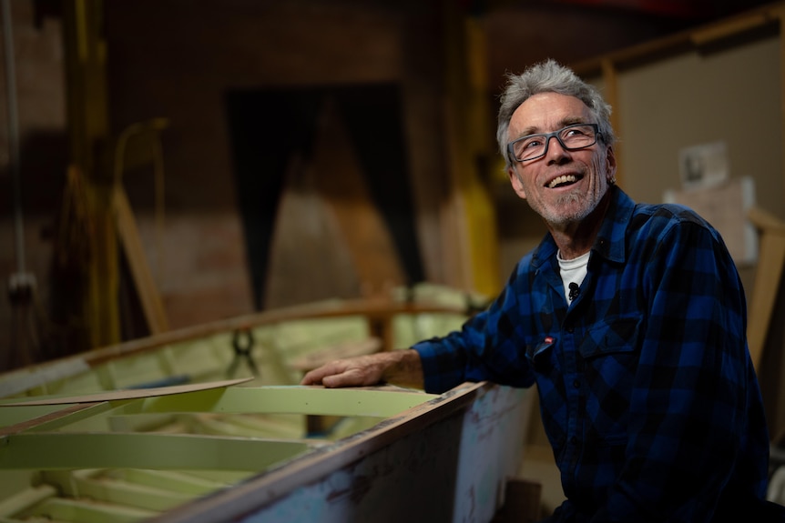 Matt Dickman smiles in front of a boat being restored.
