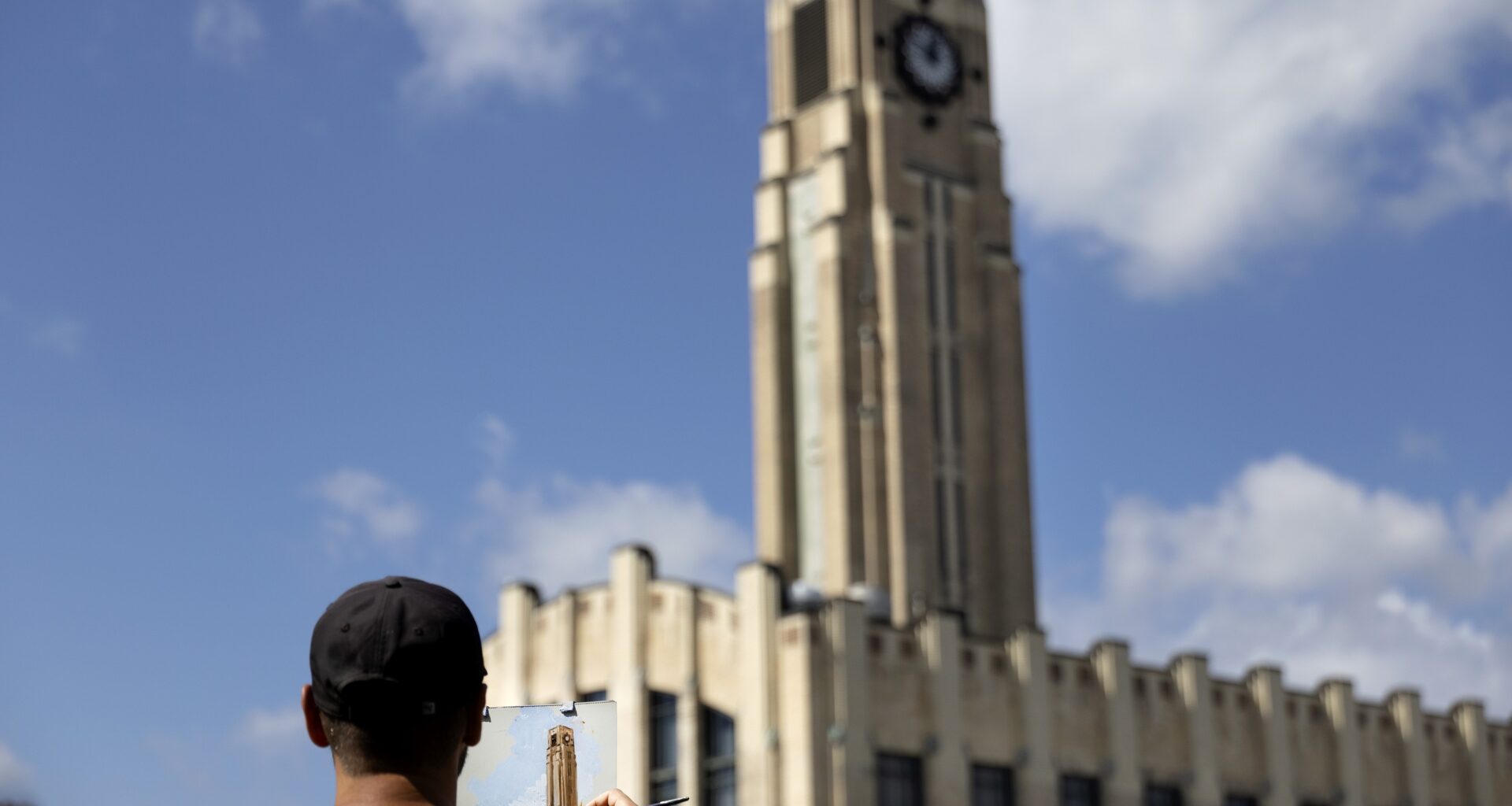 Man in front of a clock tower, painting that clock tower on an easel