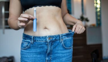 A person in jeans that are too big holds the waistband in one hand and an injector pen in the other