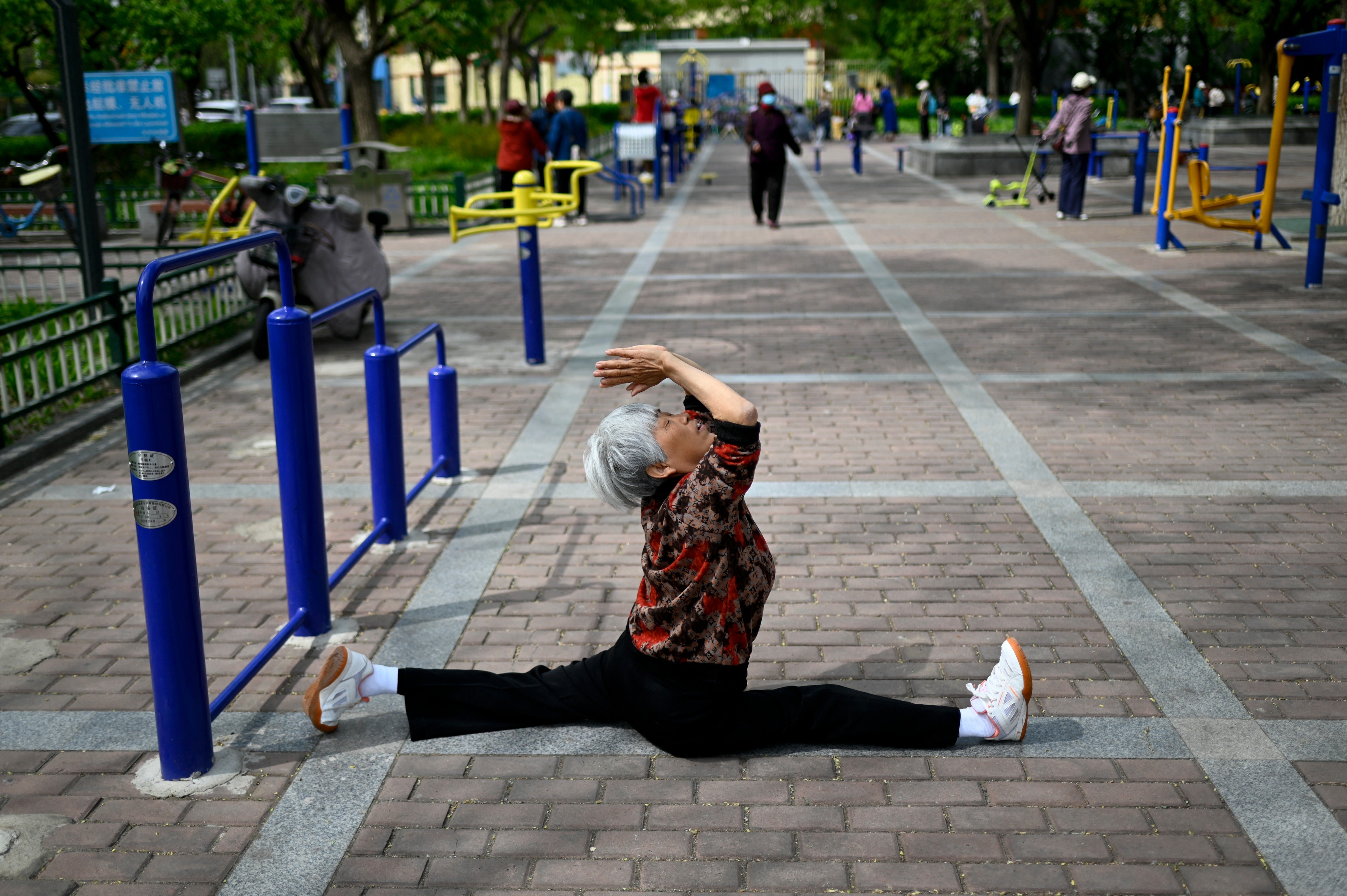 An elderly woman exercise at a public garden along a road in Beijing