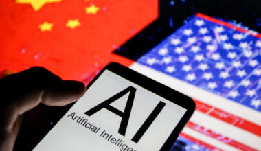 Close up view of a smartphone displaying the words AI Artificial Intelligence in front of blurred flags of the United States and China illustrating technological competition between the two countries.