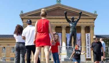 Visitors wait in line to take photos in front of the Rocky statue while a fence surrounds the statue before its installation begins in Philadelphia on Friday, Sept. 11, 2026. Access to the statue at the top of the Philadelphia Museum of Art steps will be temporarily closed for the duration of the work. Rocky will remain visible throughout construction, but will be secured behind barricades limiting access.