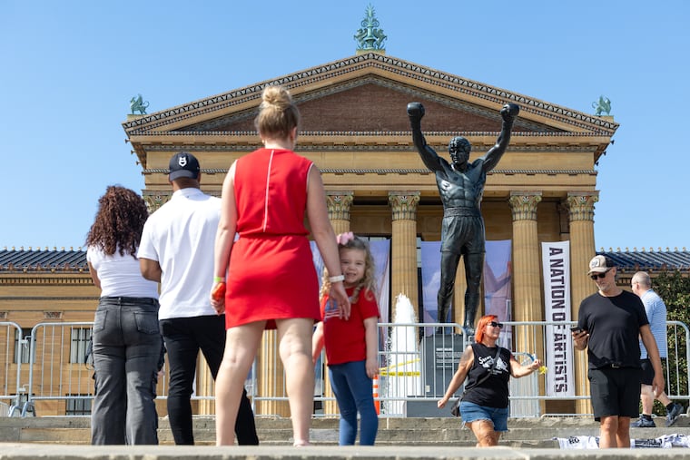 Visitors wait in line to take photos in front of the Rocky statue while a fence surrounds the statue before its installation begins in Philadelphia on Friday, Sept. 11, 2026. Access to the statue at the top of the Philadelphia Museum of Art steps will be temporarily closed for the duration of the work. Rocky will remain visible throughout construction, but will be secured behind barricades limiting access.